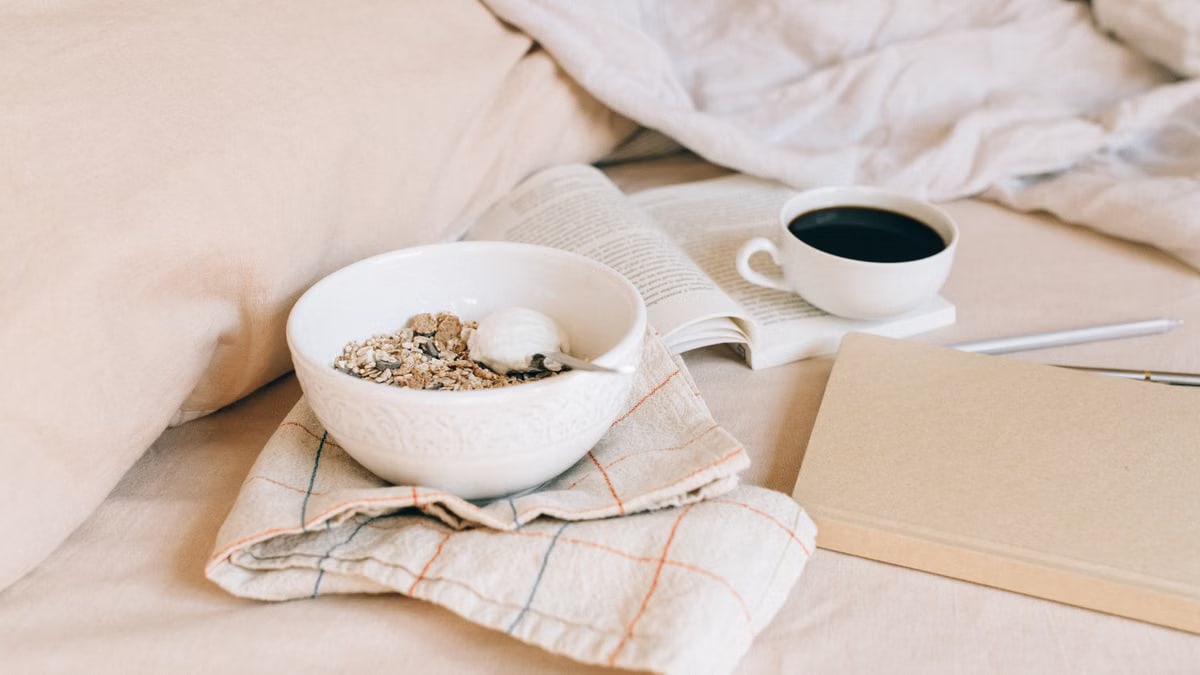 A cozy morning scene featuring a bowl of granola, coffee, and an open book on soft fabrics.